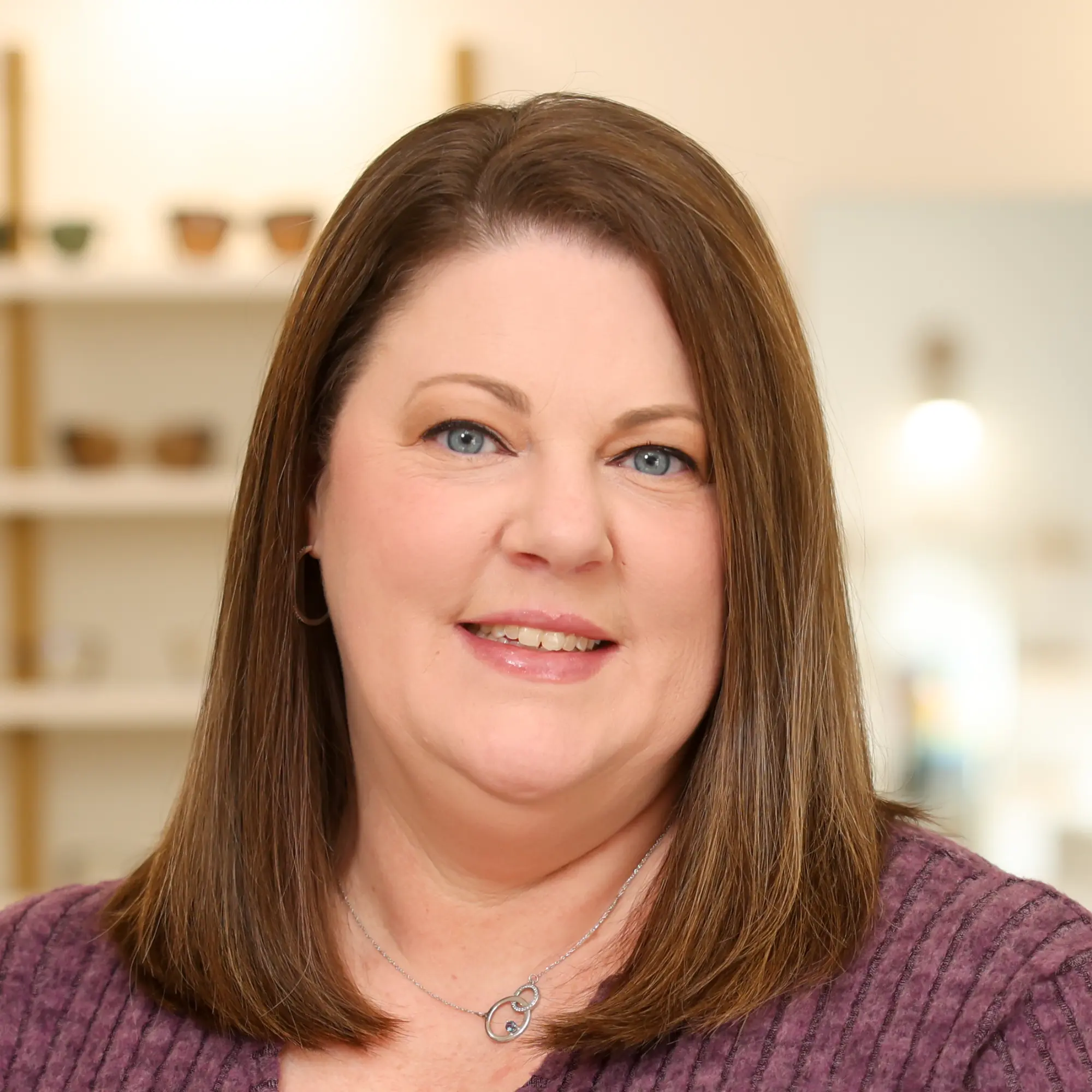 April Jobe, Insurance Specialist, smiles warmly in a purple sweater, standing in an office setting.