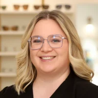 A smiling Emily Kaczynski, Optometric Technician, with blonde hair and square glasses, stands in the store showroom.
