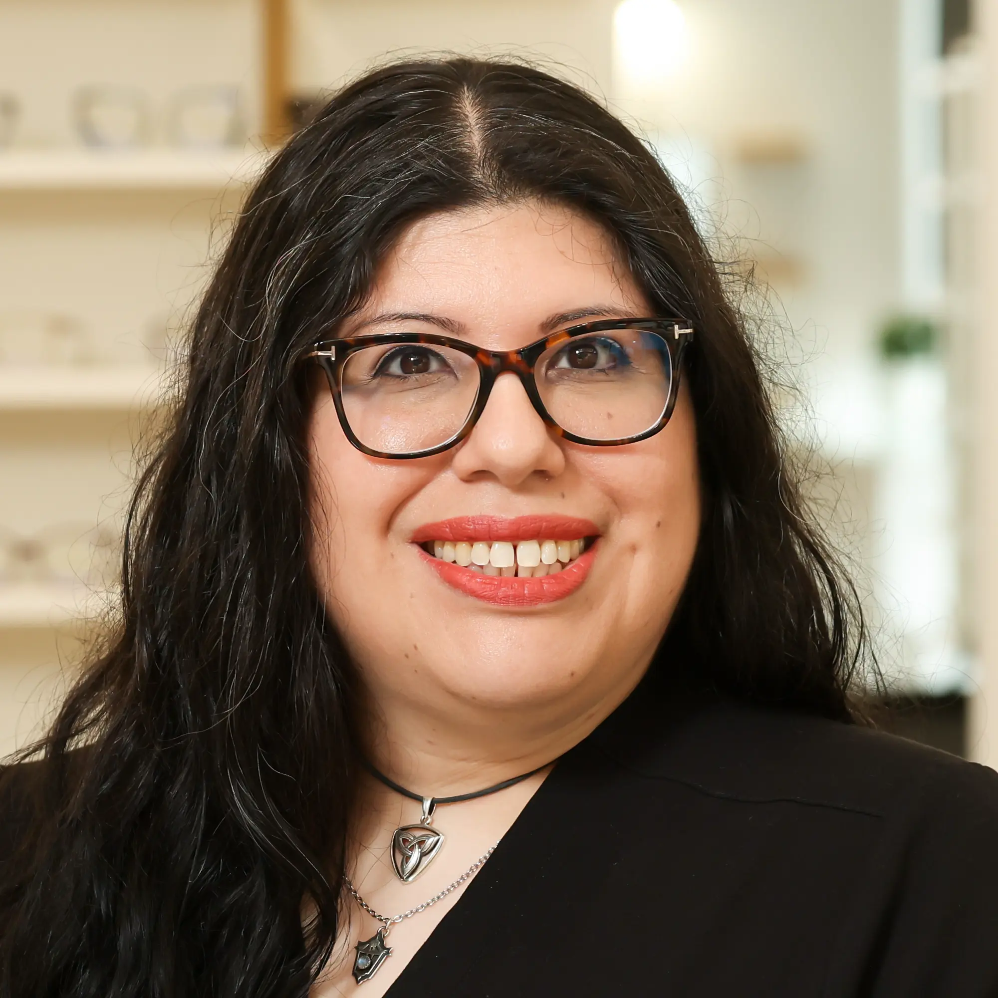 Danielle Rodriguez, an Optometric Technician, smiles in a headshot. She wears tortoise-shell glasses, a black top, and layered silver necklaces.